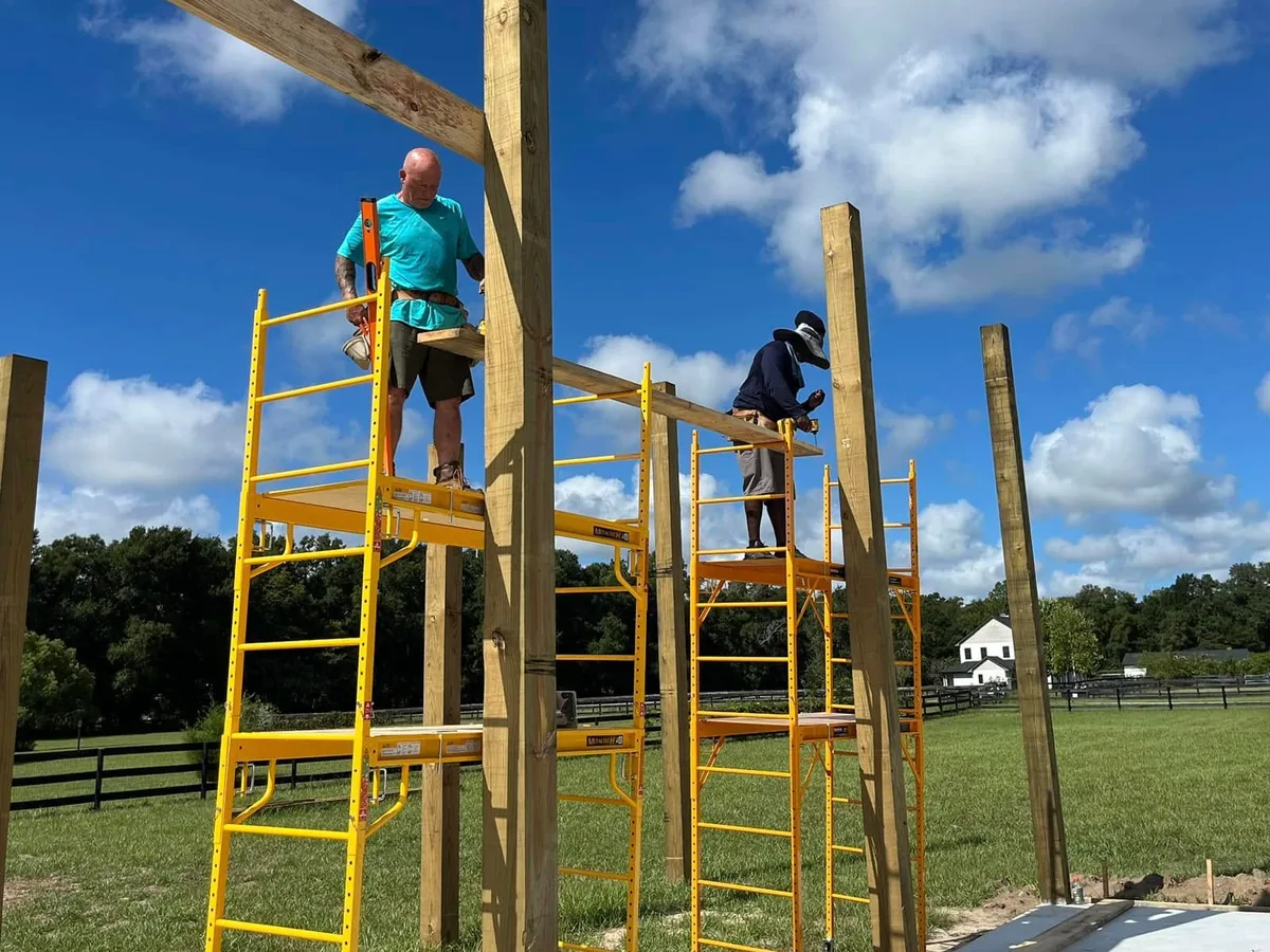 Two crew members on scaffolding setting a beam on pole barn posts