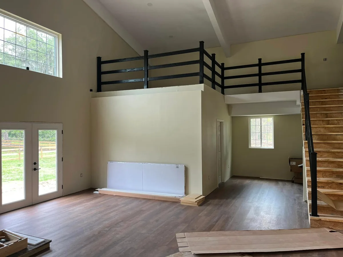 Open great room of a barndominium with a loft railing, stairs and french doors