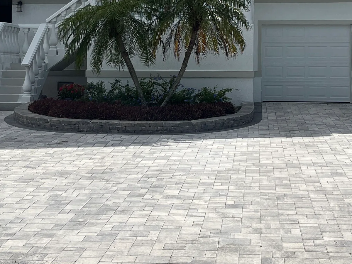 Gray concrete paver driveway with a curved planter border in front of a stucco home