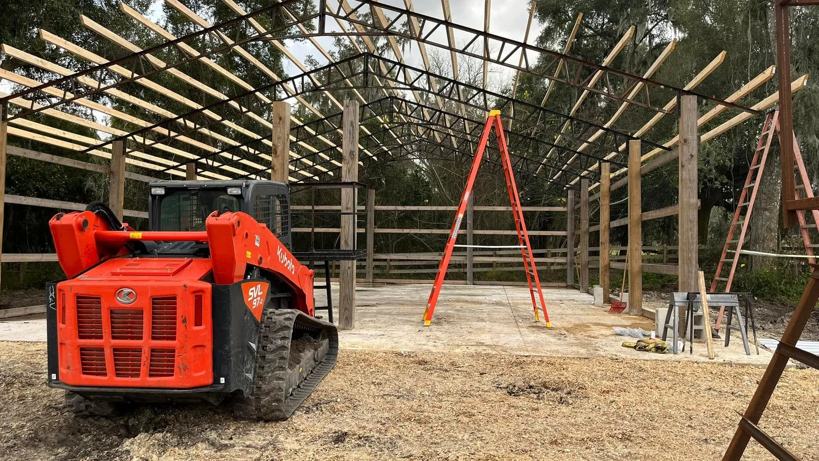 Track loader parked inside a steel truss pole barn frame on a new slab