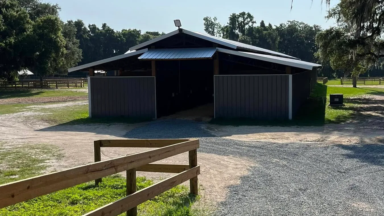 Finished horse barn with a board fence and gravel drive under live oaks