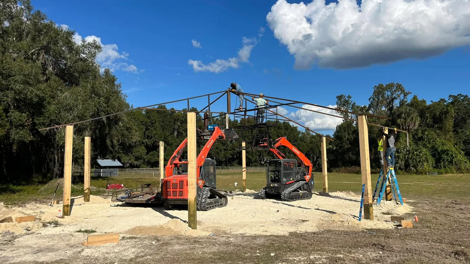 Crew and two track loaders raising the steel frame of a covered round pen