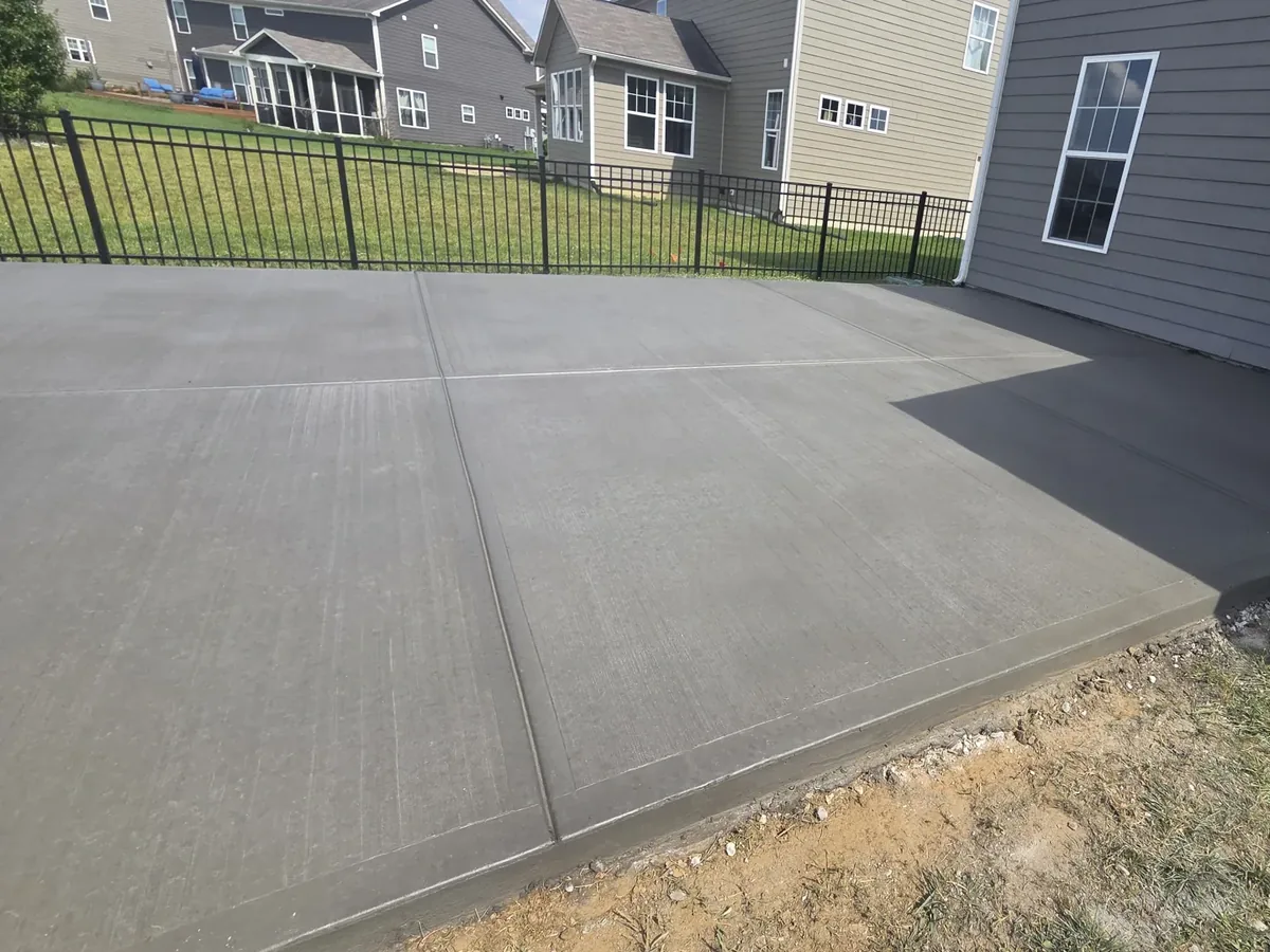 Freshly poured broom finish concrete patio with control joints beside a house
