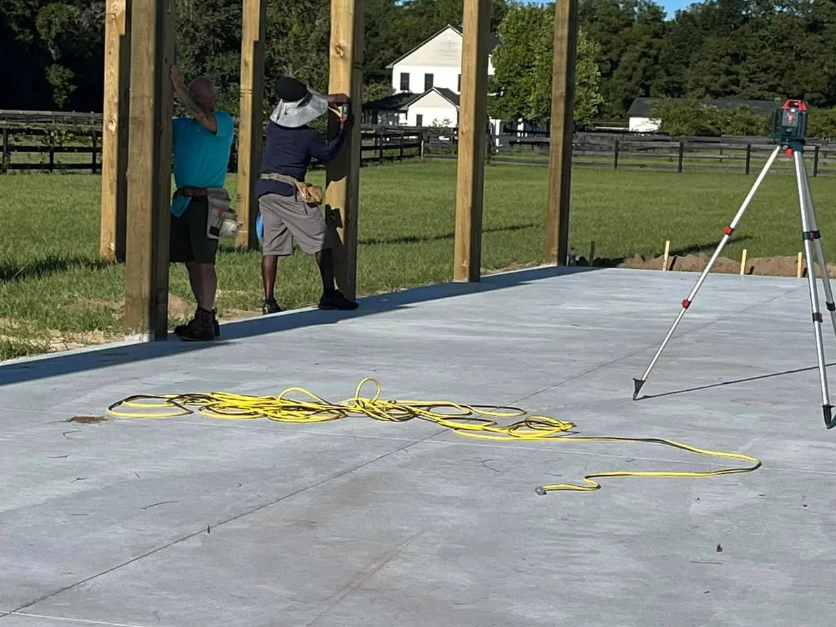 Finished concrete barn slab with posts set and two crew members measuring