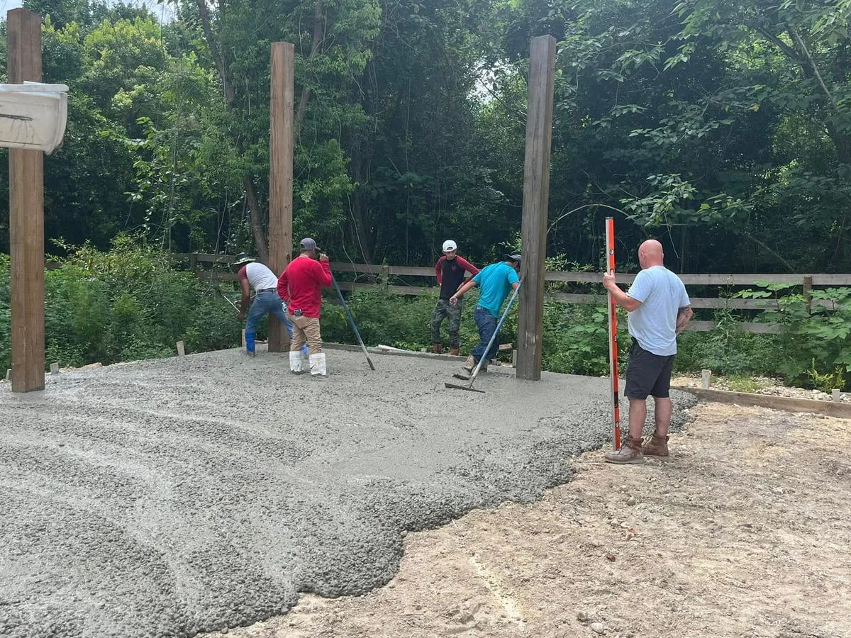 Crew spreading wet concrete between barn posts during a slab pour