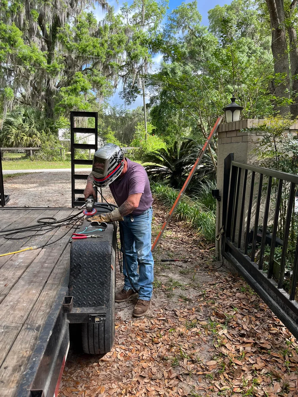Welder repairing the hinge on a farm driveway gate