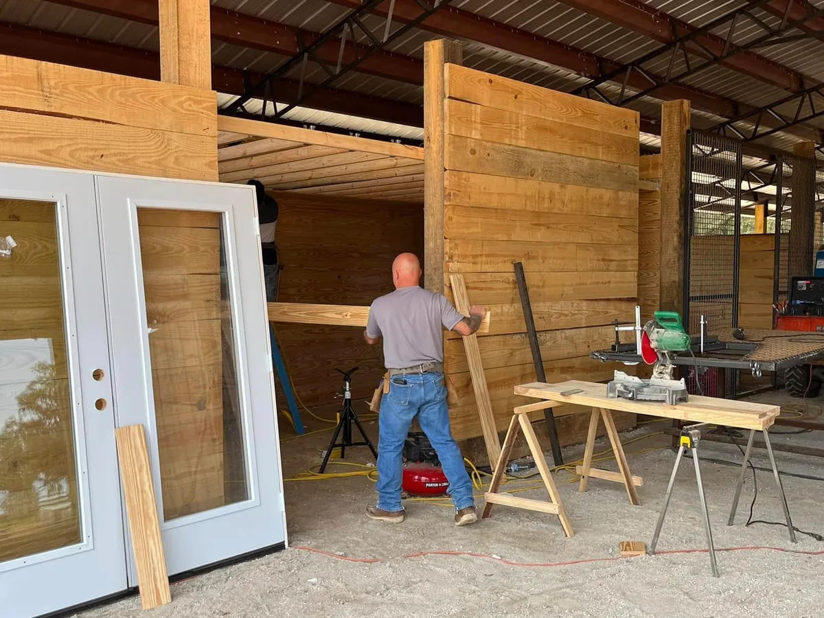 Crew cutting boards to build stall walls under steel trusses