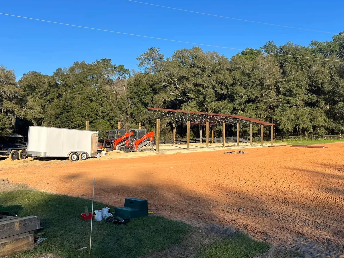 Freshly graded clay pad in front of a barn frame with track loaders