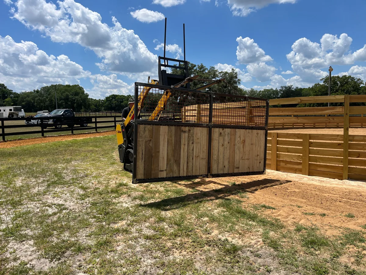 Skid steer carrying a pen panel beside a new board round pen